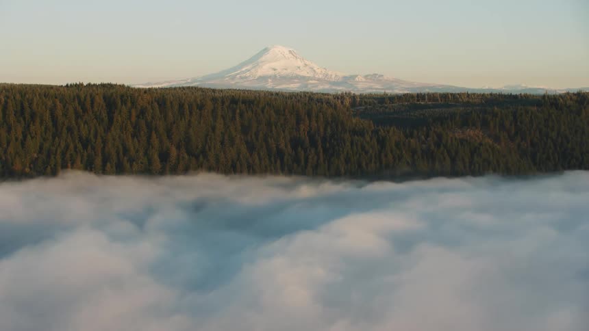 Hyperlapse timelapse flying low over morning fog with massive snow covered mountain in the background