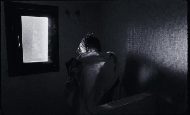 A man is standing in a sauna drying himself with a towel and looking out a window