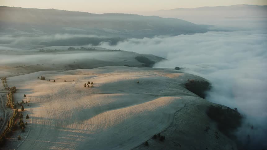 Golden morning sun illuminates wheat fields as fog rolls in over rural river valley in early morning winter light in this aerial
