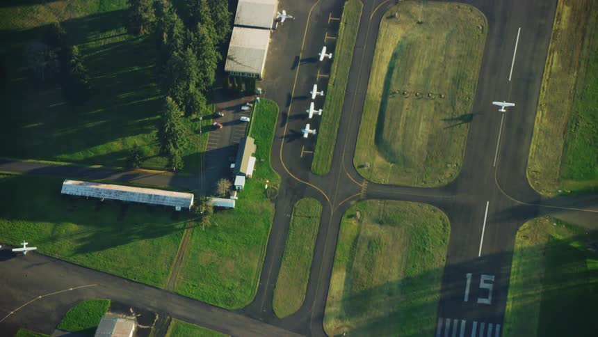 An aerial view of a single engine airplane landing on a runway in warm and golden evening sunlight with a nice airplane shadow on landing