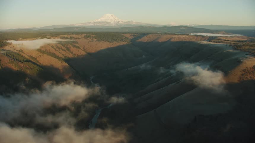 Clouds sit low over pristine river valley with Mount Adams in the background in the Cascade Range