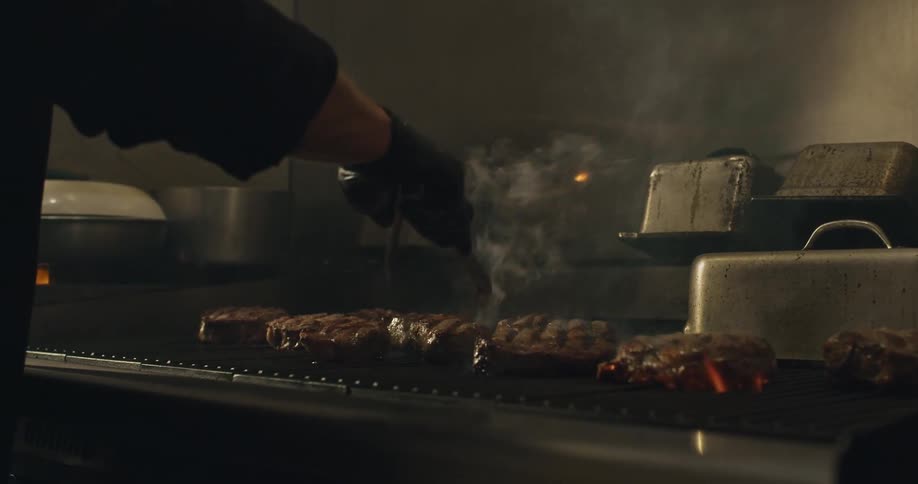 A person is flipping and grilling steaks on a commercial stove top