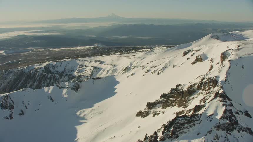 Flying over the flanks of a massive volcano with another snow covered mountain in the background