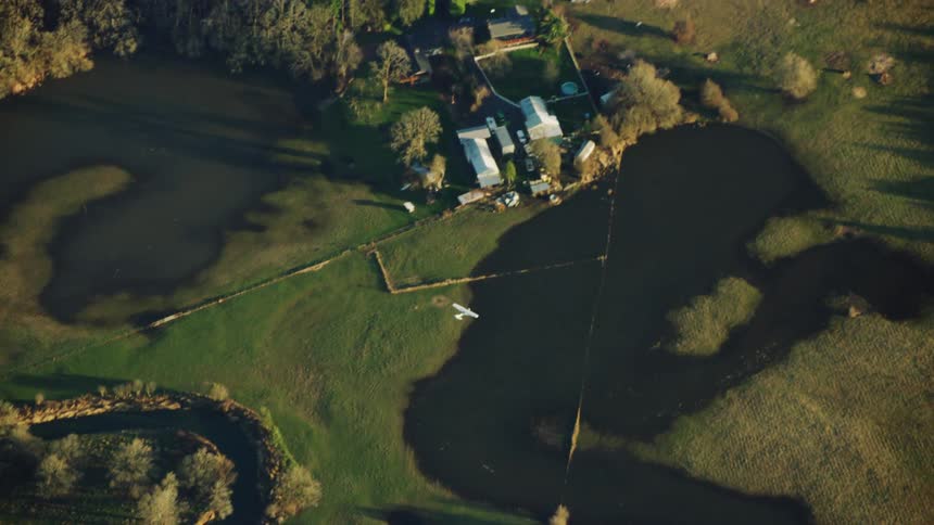 Aerial view of a white single engine airplane flying over rural countryside in the evening