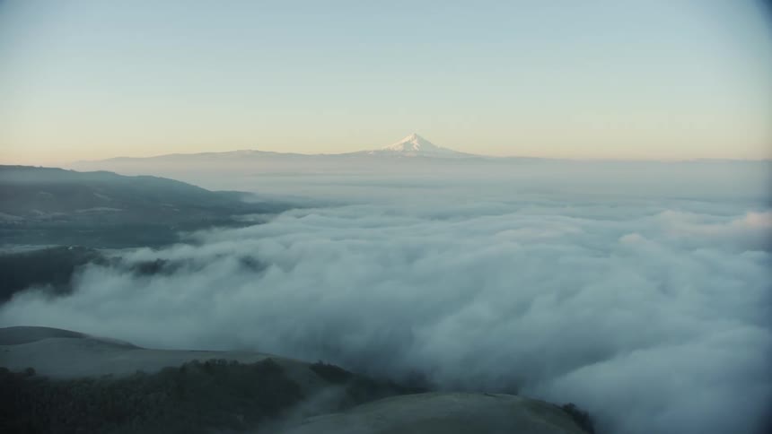 Early morning fog fills in river valley with massive snowy mountain in the background