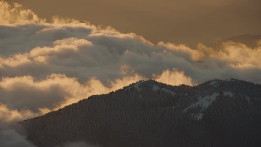 White clouds rolling over the snow covered mountains at sunset