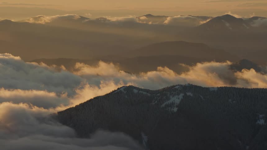 Sweeping panning shot of clouds blowing off ridge at sunset from 10000 feet above earth