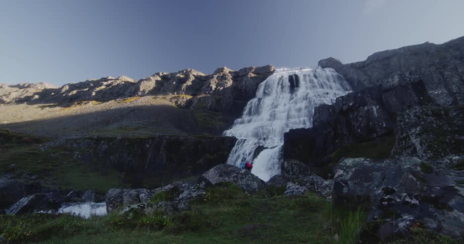 People in the distance are standing by the foot of a large waterfall