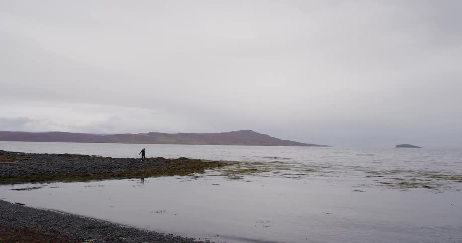 A person is walking on rocks by the shore in the distance