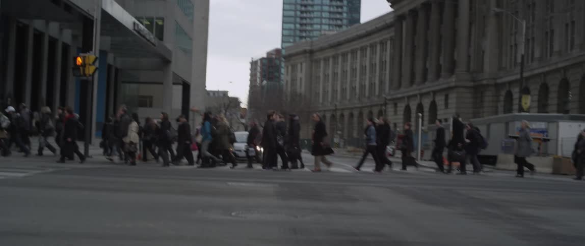 A large group of people are crossing the street in a city