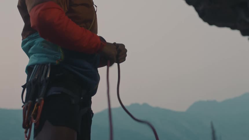 Male mountaineer coils rope on mountain