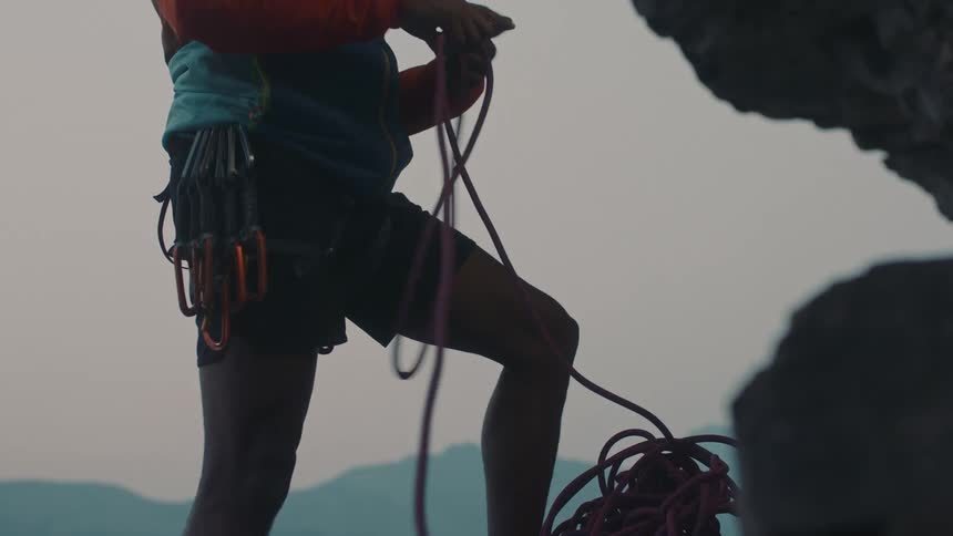 A mountain climber is on the side of a mountain pulling up his rope