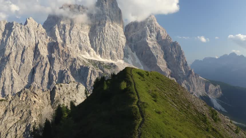 Aerial view of a path on a mountain ridge close to a mountain range covered in clouds at morning