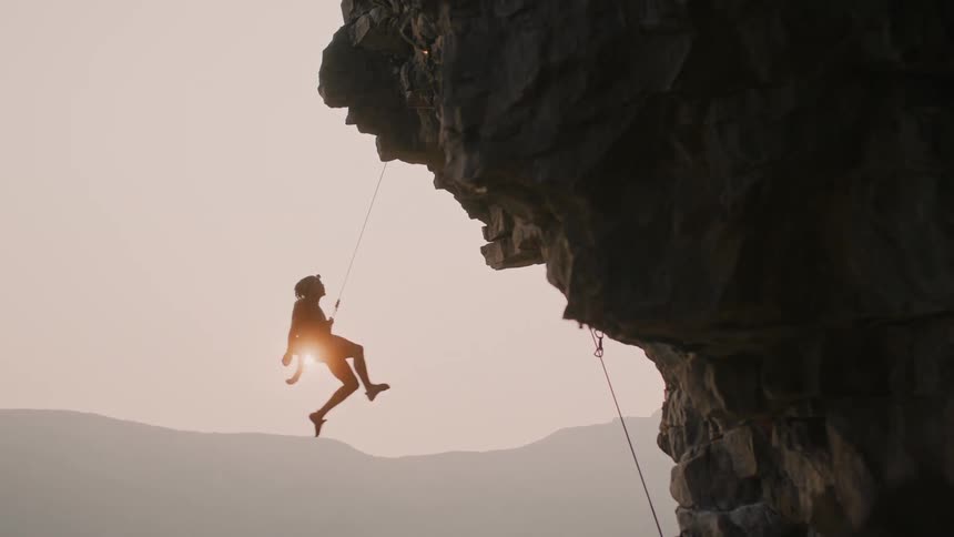 A man propels down a mountain as he rock climbs