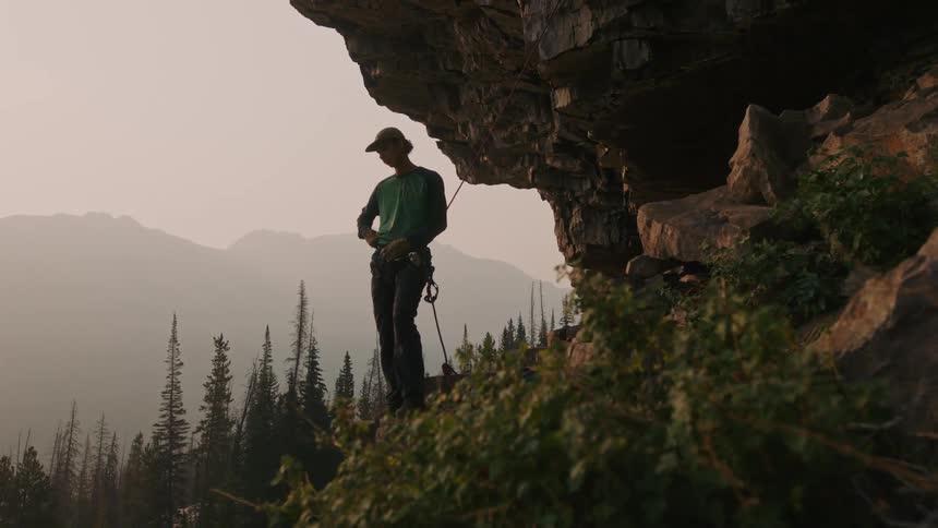 Person stands looking down mountain slope with forest and fog covered mountains in the background