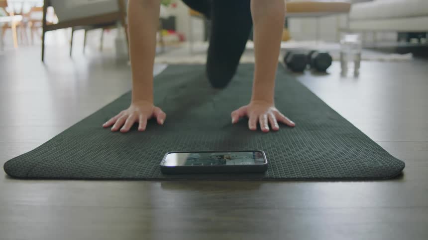 A woman works out at home while watching a video on her smartphone