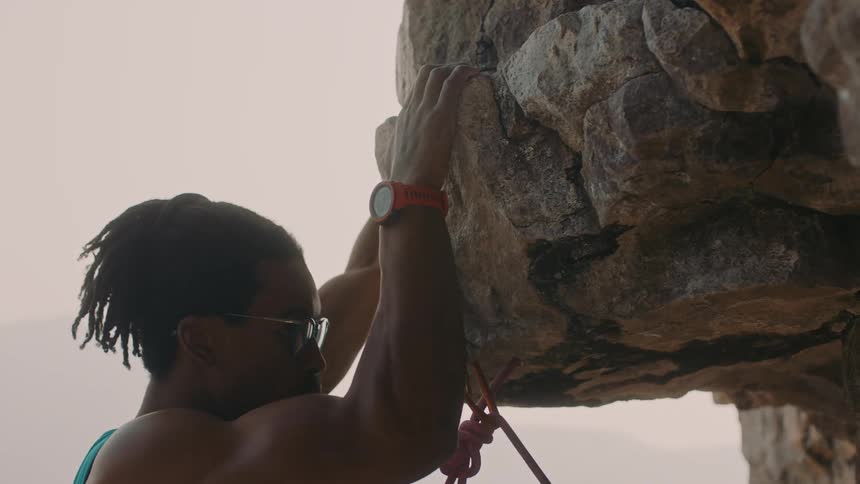 Young man wearing mountaineering gear climbing the rocky face of a mountain at sunset