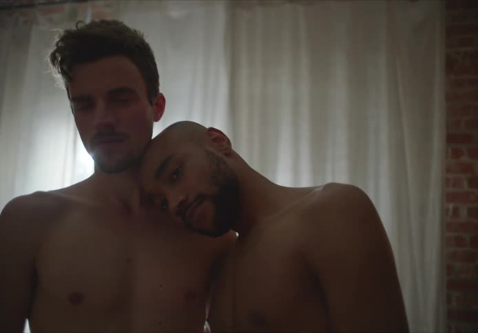 Two men stand shirtless together in the room