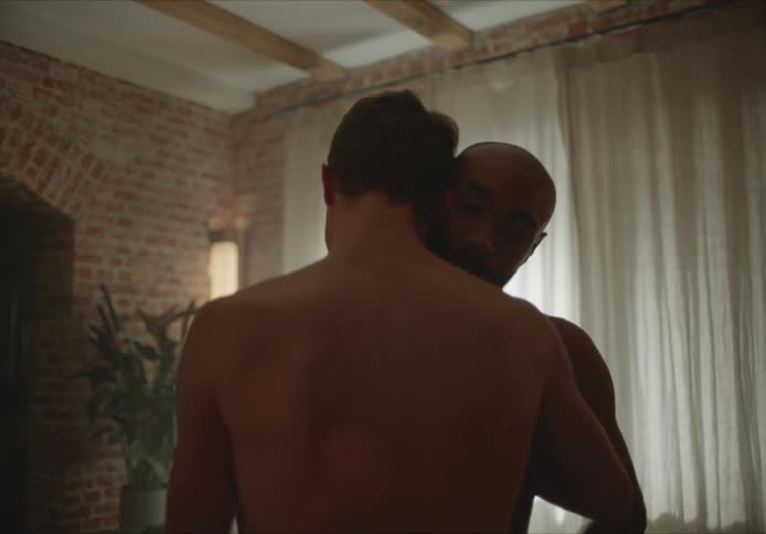 A gay male couple dancing shirtless in a living room