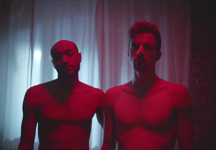 A couple standing in a room shirtless