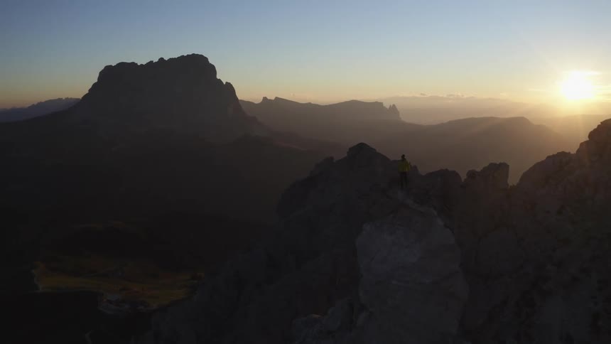 Aerial view of a man standing on the top of a mountain at sunset
