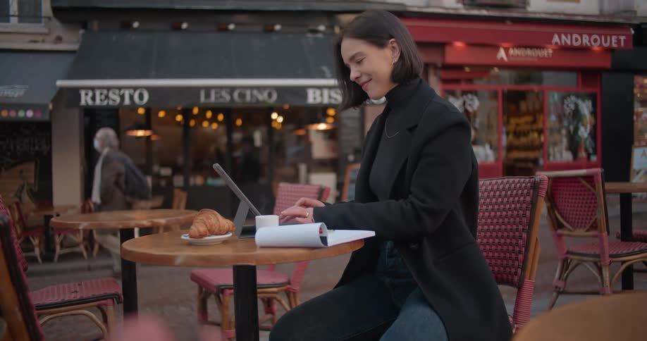 Young woman sitting on a street restaurant working on a laptop