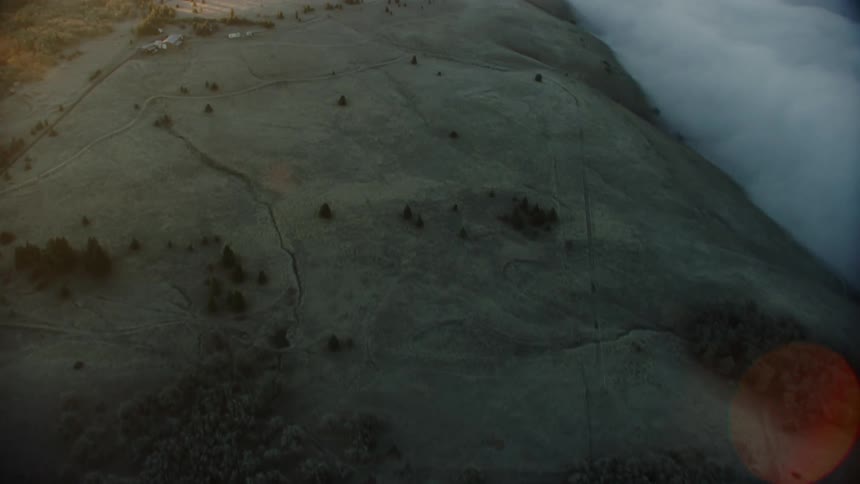 Slow tilt up from dryland wheat farming land to a vast valley filled with early morning fog at sunrise early in the morning from a helicopter aerial