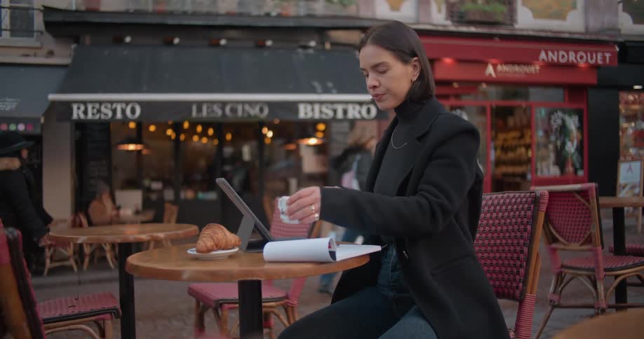 Woman sitting on a street restaurant drinking coffee and writing on a notepad