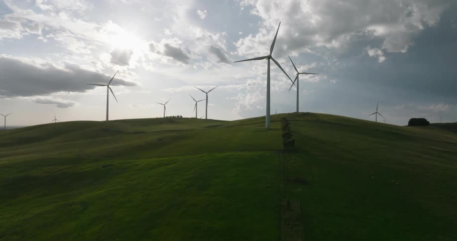 Wind turbines standing on grassy hills rotate slowly against cloudy sky