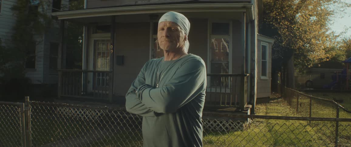 A man standing in front of a house crosses his arms in front of his chest