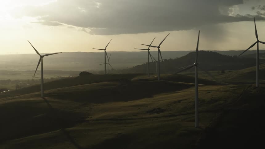 Wind turbines spinning over a hill on a wind farm at sunset