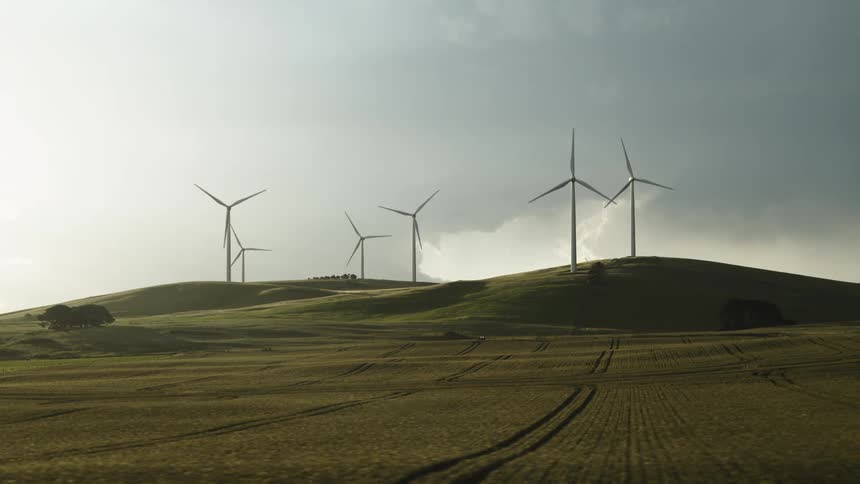 Wind turbines spinning on a wind farm on the hills near the fields at morning