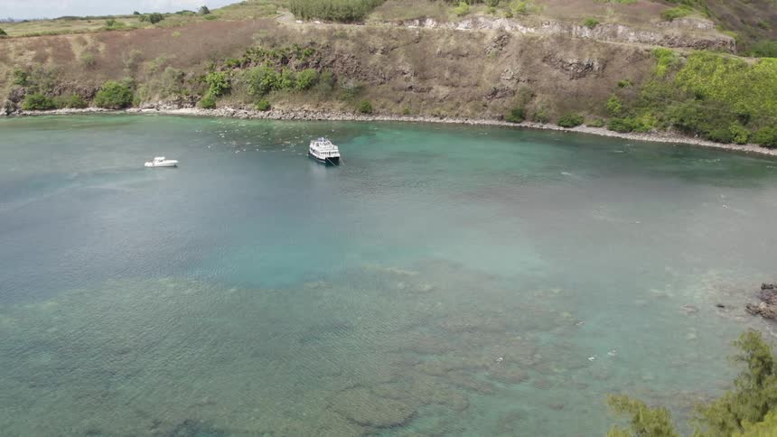 Two boats anchored just off the coast in a clear water cove