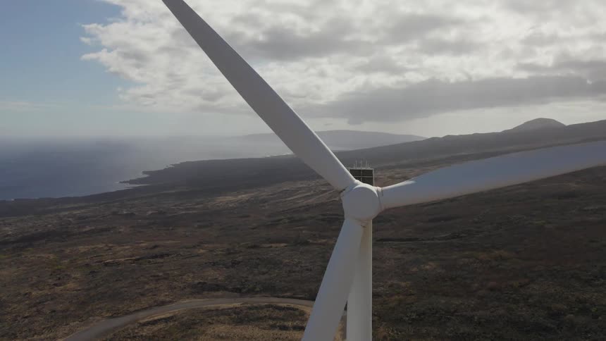 Wind turbine blades spin slowly in hilly terrain near shore on misty day