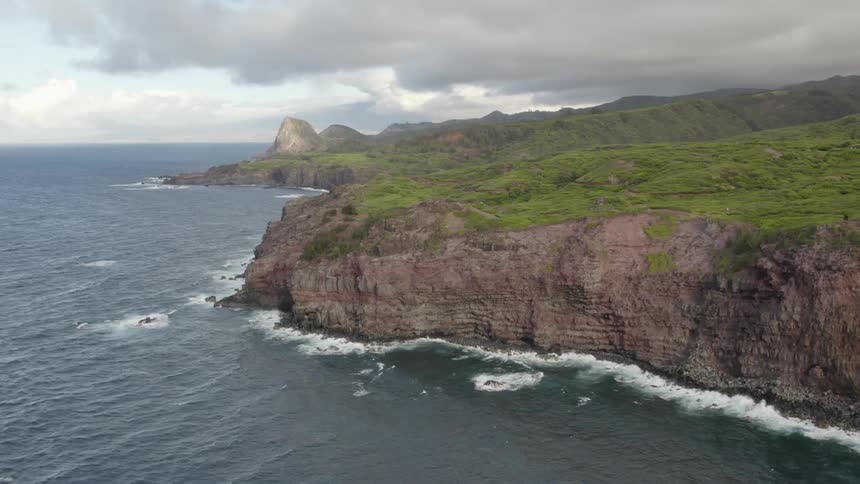 Dark clouds hover over misty land as waves crash against base of cliffs