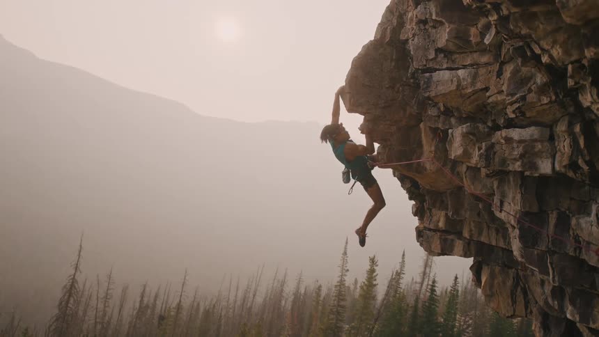 Young man wearing climbing a mountain drops down on a cliff in hanging from a rope