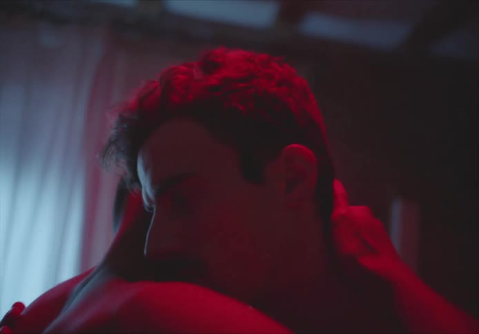 Two men without shirts hold one another closely and dance together