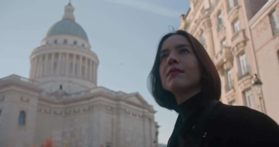 A young woman takes a picture of a government building and then looks around before walking away
