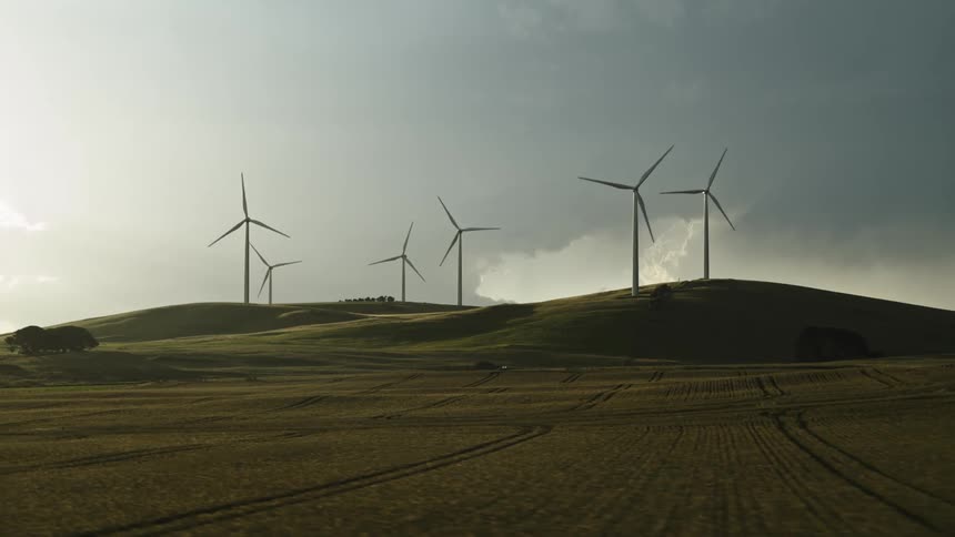 Wind turbines work in hills on wind farm under clouds