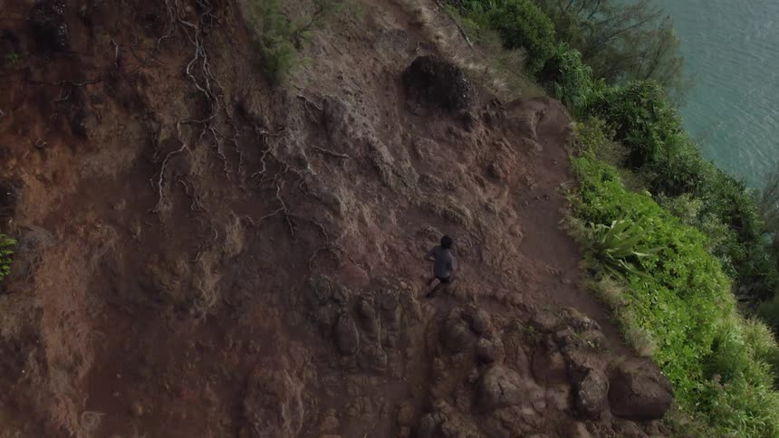 A jogger is running along the top of a headland with trees and water below