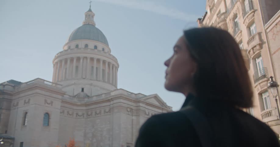 A woman stands in front of a government building and looks at it and then turns around before walking away