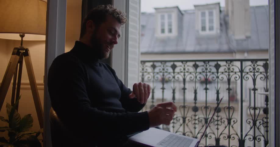 A man gestures to his laptop screen during a video call at home