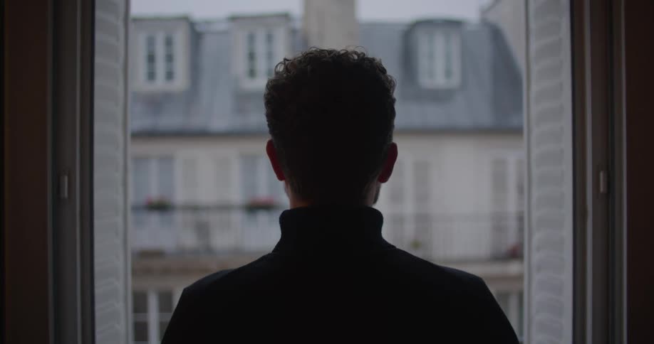 Man stands sipping from cup as he stares across to other apartments