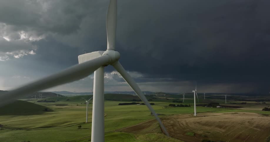 Wind turbine spinning on a wind farm in the fields close to storm clouds