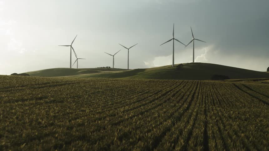Wind turbines spinning on a wind farm in the hills close to a field in a farm at morning