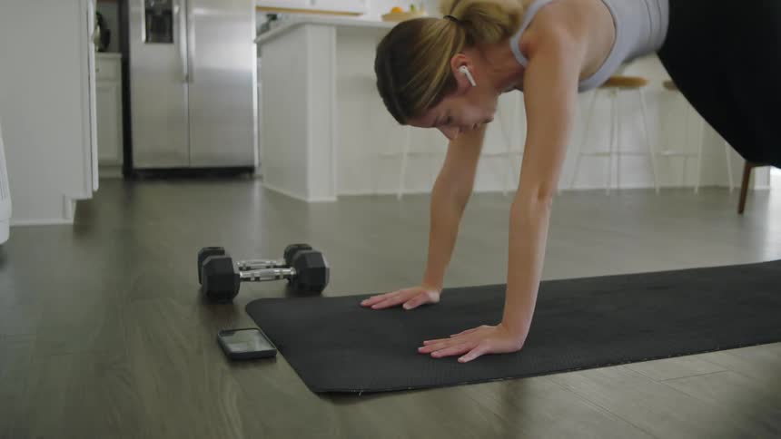 Young fit woman wearing sports clothes working out over a mat on the kitchen at home