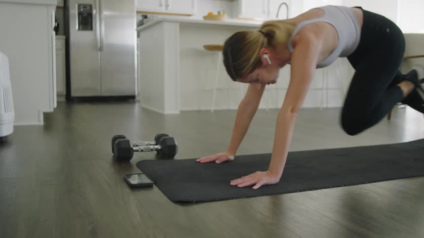 Young fit woman wearing sports clothes working out over a mat on the kitchen at home