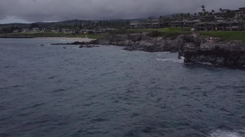 Strong waves crash onto rocks along a coastal neighborhood