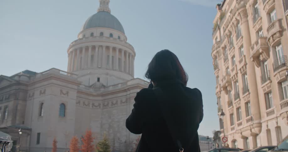 A woman is taking a picture of a building with a dome on top