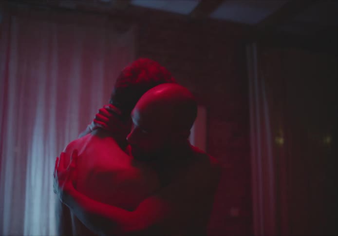 Male couple hugs as they slow dance in dim room lit by red light